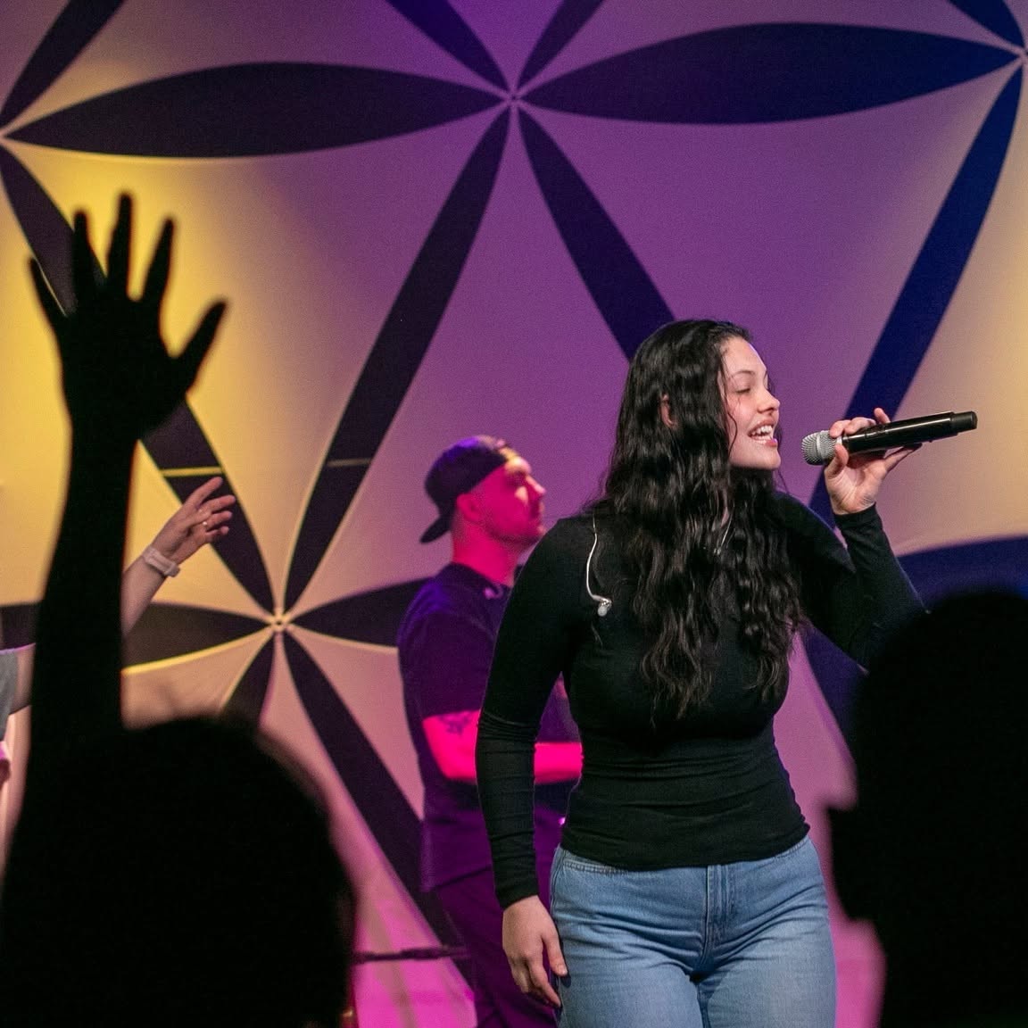A young woman leading worship as people raise their hands at Revolution Church in Salina, Kansas
